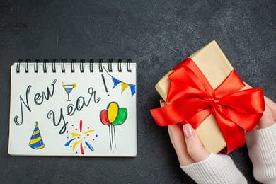 top-view-hand-holding-beautiful-gift-with-bow-shaped-ribbon-dark-background_140725-60535 new year